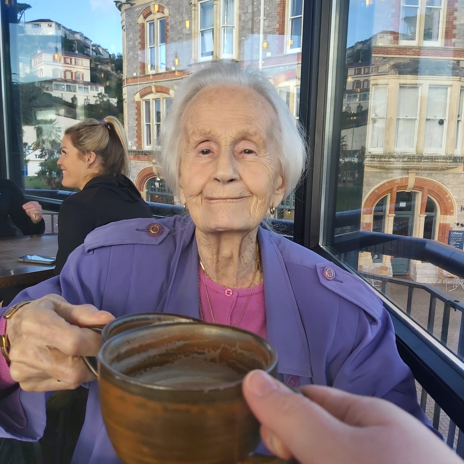 A Brand Partner sharing a warm drink and a toast with a client at a harbour café